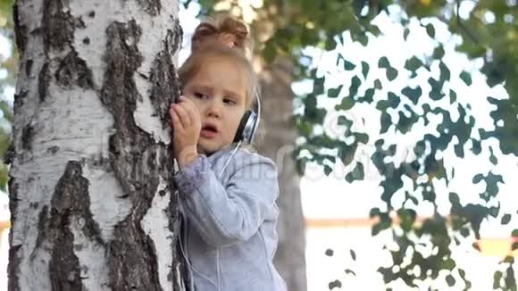 婴儿戴着耳机听音乐在公园里用桦树唱歌视频的预览图