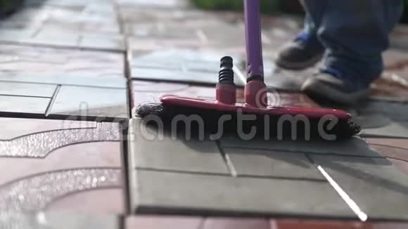 一个小男孩在花园里用拖把帮助家人清理瓷砖慢动作视频的预览图