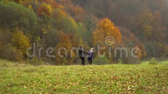 一位年轻的母亲和她的小女儿在秋天的森林里玩耍妈妈和女儿快乐地旋转着牵着手视频的预览图