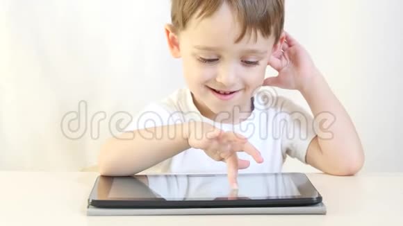 一个快乐的孩子正坐在一张桌子旁在平板电脑上玩脸上带着微笑这孩子正在玩电子游戏视频的预览图