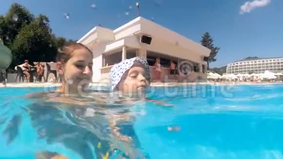 年轻母亲在酒店度假村的游泳池里教她蹒跚学步的儿子游泳的慢动作镜头视频的预览图