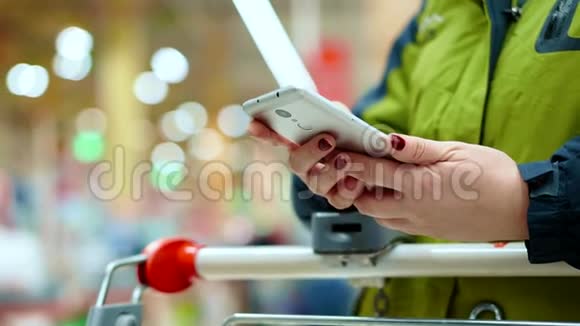 超市里的一位女士手里拿着一部智能手机她正靠在一个装满货物的篮子上等着排队视频的预览图