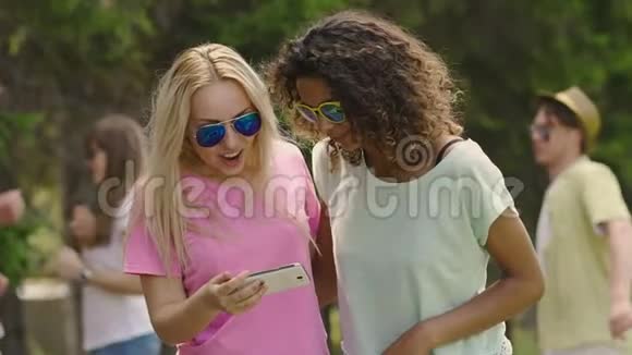 年轻漂亮的女人在公园里的智能手机上看照片聚会放松视频的预览图