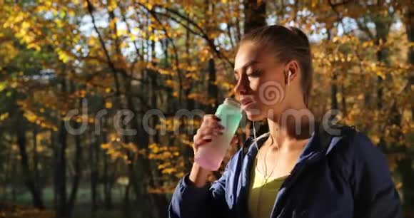 公园里的女跑步者女人喝着水站在秋天的公园里满是落叶视频的预览图