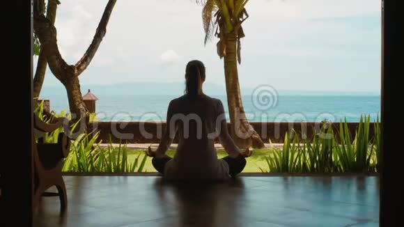 从海边的平房里在莲花的位置练习瑜伽让女人放松的剪影美丽的景色自然的声音视频的预览图