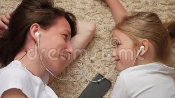 有趣的画面年轻女子和小女儿躺在地板上互相看着对方听着音乐视频的预览图