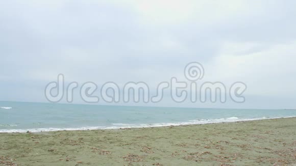 狂风暴雨的海边天边灰云密布年轻的黑发女人在海滩上奔跑视频的预览图