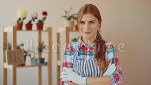 小生意一个穿着条纹围裙和格子衬衫的女孩站在花店里双手叠在胸前视频的预览图