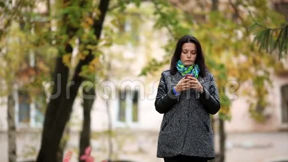 快乐的黑发女人站在公园里用智能手机视频的预览图