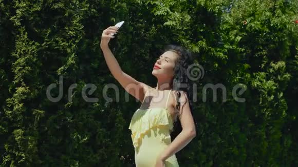 美丽卷曲红唇黑发女郎在绿树背景下自拍视频的预览图