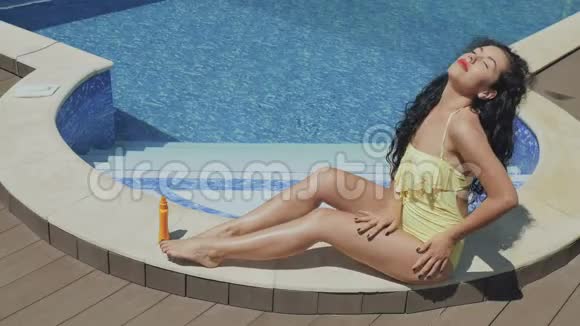 在游泳池附近一个漂亮的卷发黑发女人用化妆水给自己抹上一层视频的预览图