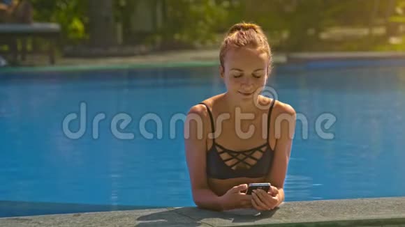 带现代智能手机的金发女孩在泳池旁视频的预览图