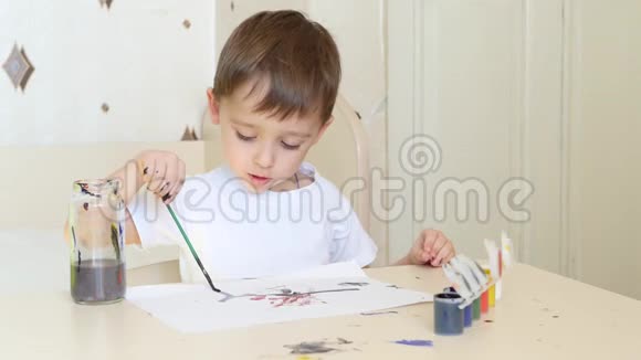 一个小男孩坐在桌子旁用画笔在一张纸上画画水彩颜料视频的预览图