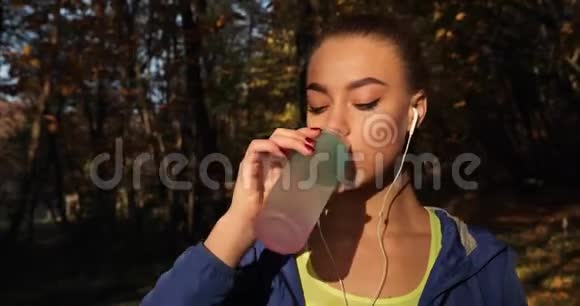 公园里的女跑步者女人喝着水站在秋天的公园里满是落叶视频的预览图