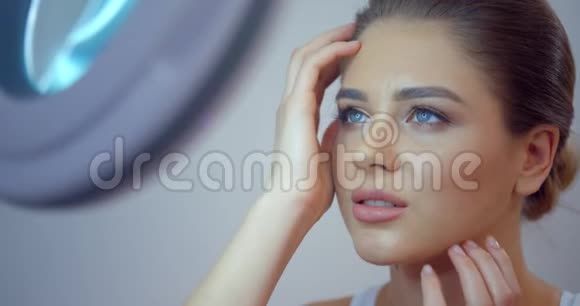 漂亮的年轻蓝眼睛女孩有着瓷质的新鲜皮肤和天然的妆容正在欣赏她的镜子4k个镜头视频的预览图