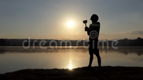 日落时分快乐的人在湖岸摇着他的冠军碗视频的预览图