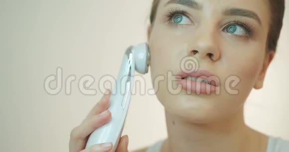 迷人的年轻女性自然化妆正在按摩她的脸与电动液化石油气工具在白色背景4k视频的预览图