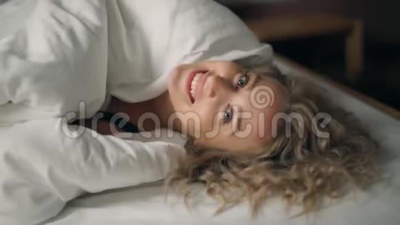 在家里微笑着快乐的女孩从毯子下偷看亲吻相机视频的预览图