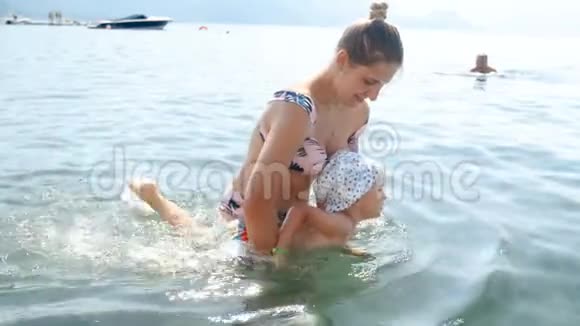 4k视频年轻母亲教她蹒跚学步的孩子在海里游泳视频的预览图