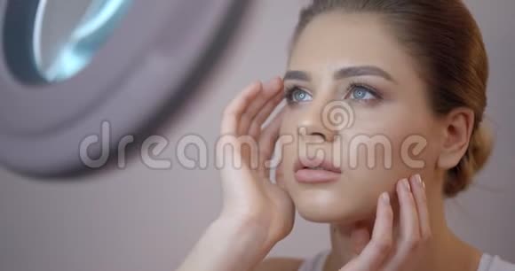 皮肤护理年轻的蓝眼睛女孩摸着她的脸照着镜子她在欣赏她的样子4K录像关闭视频的预览图