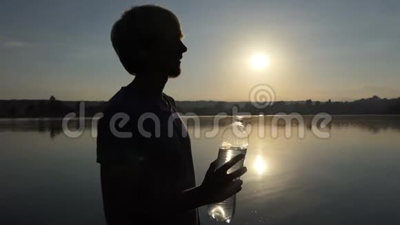 时髦的男人在日落时举起一个塑料瓶子喝水视频的预览图