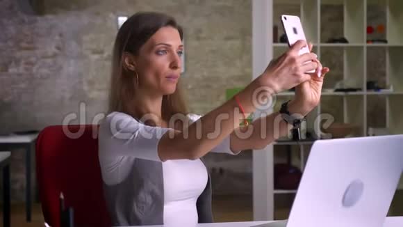 有魅力的女办公室工作人员在室内工作场所在笔记本电脑前自拍视频的预览图