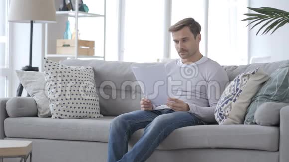 Penve成年男子边坐沙发边看文件视频的预览图