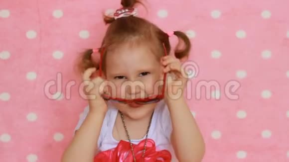 有趣的孩子微笑笑露出舌头粉色背景可爱的小女孩戴着红墨镜的心形图案视频的预览图