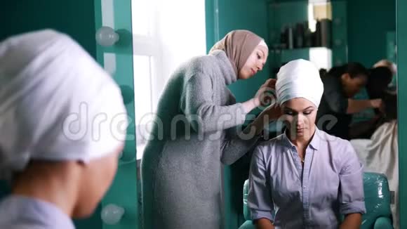 靠近镜子的穆斯林妇女将伊斯兰头巾系在漂亮的新娘身上视频的预览图
