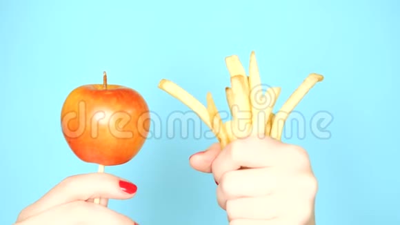 健康和不健康食品的概念一个苹果放在明亮的蓝色背景上的炸薯条上红色的女性手视频的预览图