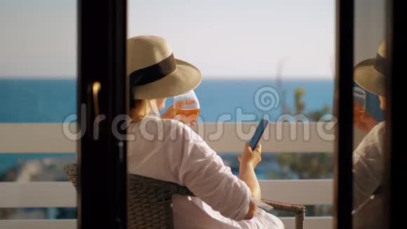 在俯瞰大海的阳台上放松时带酒杯的女士使用牢房视频的预览图