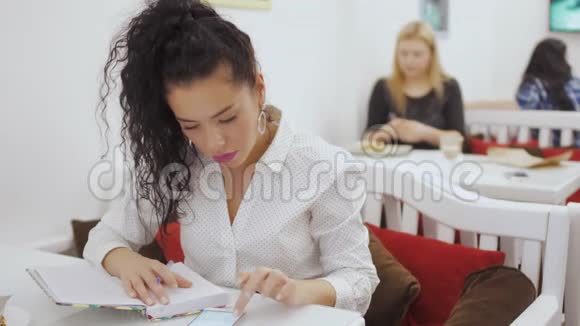 年轻漂亮的黑发女郎在笔记本上计划她的一天在咖啡馆里放松视频的预览图
