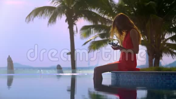 女孩使用桌坐在池边与棕榈树特写视频的预览图