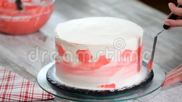 甜点手抹粉红色奶油白色糖霜海绵蛋糕在木制转盘在面包店厨房关闭视频的预览图