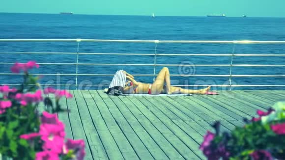 在大海和船只的背景下女人躺在木船甲板上的花朵附近晒日光浴视频的预览图