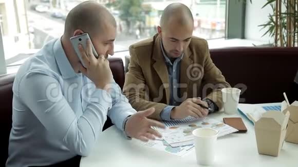 两个年轻人在一家咖啡馆吃午饭喝咖啡吃面条讨论生意工作食物电话视频的预览图
