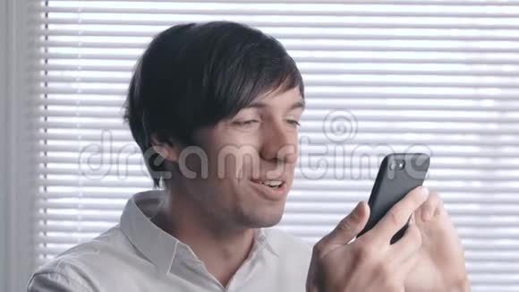 一位微笑的年轻商人的画像在百叶窗的背景下使用智能手机视频的预览图