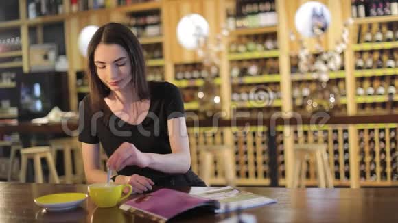 一个年轻的女孩喝咖啡在咖啡馆或餐馆看时尚杂志女人读杂志喝酒视频的预览图