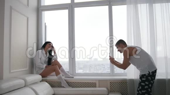 幸福的年轻家庭夫妇在家哈斯班德在窗户上拍了他妻子的照片冬天下雪了视频的预览图