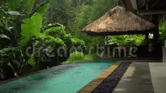 热带森林中的慢动作雨开放的游泳池和茅草屋复制空间视频的预览图