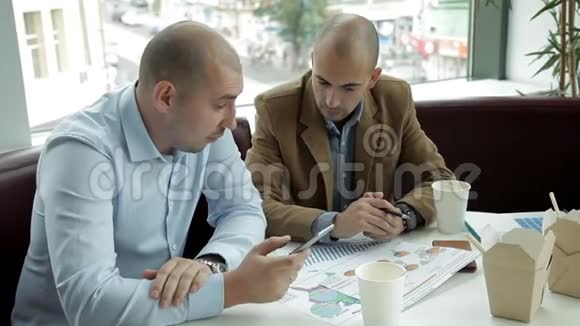 两个年轻人在一家咖啡馆吃午饭喝咖啡吃面条讨论生意工作食物电话视频的预览图