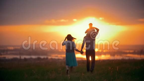 快乐的家庭户外妈妈爸爸和小儿子在夏日草地散步到日落视频的预览图