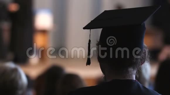 卷发男子穿着灰泥板和学术服装看舞台毕业视频的预览图