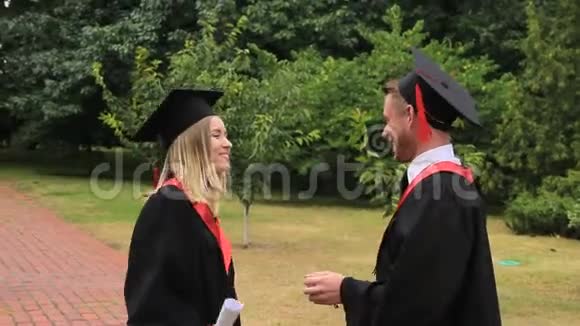 快乐的毕业生拿着毕业证书在学院附近的公园拥抱快乐视频的预览图