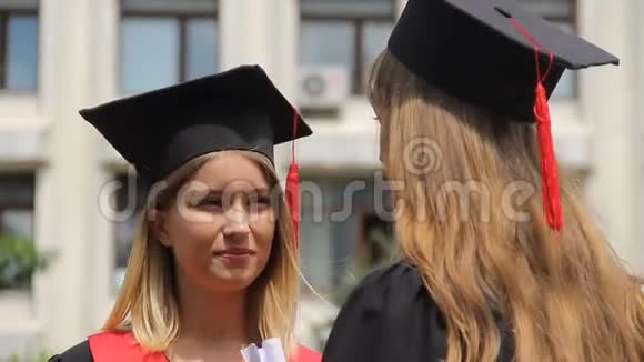 戴着学术帽的金发女人在毕业典礼上聆听最好的朋友视频的预览图