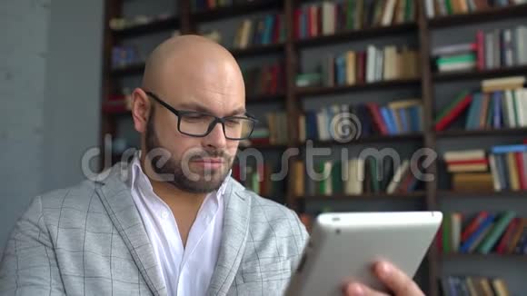 戴眼镜的年轻人使用平板电脑上网戴眼镜的年轻人在家里工作背景是视频的预览图