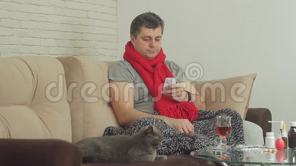 一个有感冒迹象的人用毯子盖着坐在沙发上用视频的预览图