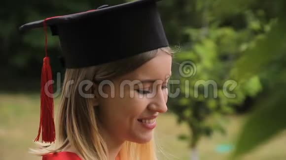 年轻的金发女郎穿着学术服装打电话留言毕业典礼视频的预览图