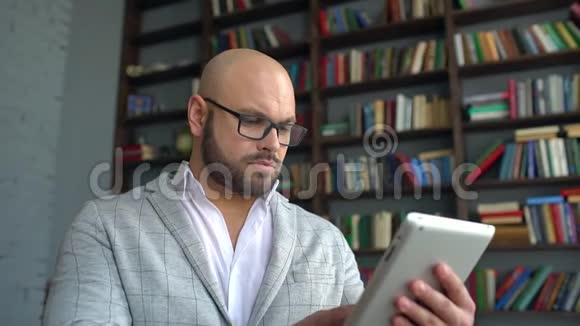 戴眼镜的年轻人使用平板电脑上网戴眼镜的年轻人在家里工作背景是视频的预览图