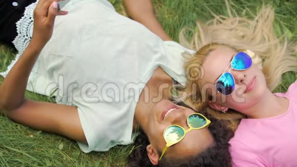 戴太阳镜的女士享受夏天躺在草地上在智能手机上上网视频的预览图